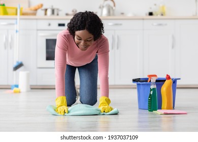 Happy african american young woman cleaning floor in kitchen