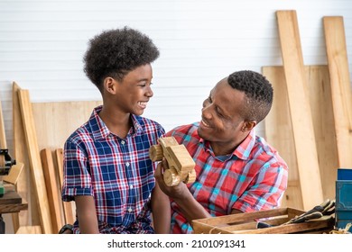 Happy African Black Male Carpenter Man Father And Boy Kid Child Son With Wooden Toy Car Model Present Gift In Carpentry Workshop. Concept Hobby At Home.