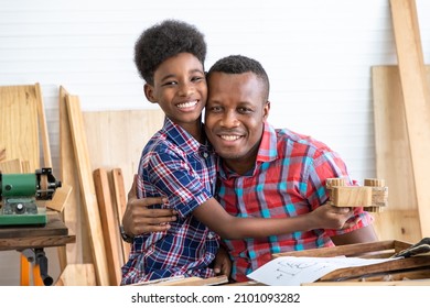 Happy African Black Male Carpenter Man Father And Boy Kid Child Son With Wooden Toy Car Model Present Gift In Carpentry Workshop. Concept Hobby At Home.