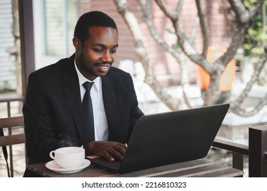 Happy African Businessman In A Suit Use Business Laptop At Coffee Shop. Smiling Black Male Executive Typing Business Email On Computer At Corporate Desk, Surfing The Web, Online Work In Office