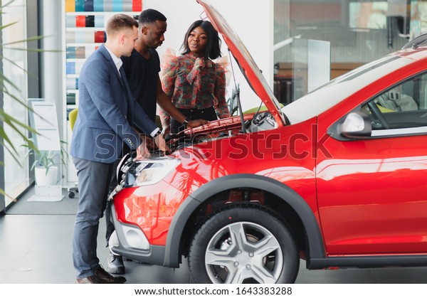 happy african car salesman showing car engine\
to customers