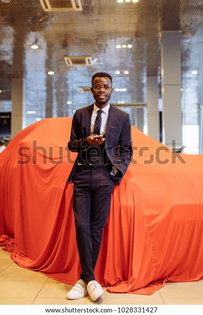 happy\
african car salesman using smart phone in\
showroom