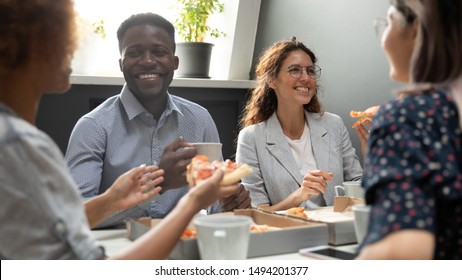 Happy African And Caucasian Business Team People Sharing Pizza In Office, Friendly Diverse Multiracial Staff Employees Talking Laughing Eating Dinner Food Meal Together Having Fun At Corporate Party