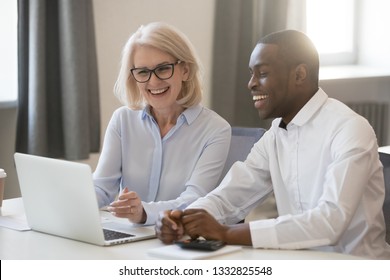 Happy African And Caucasian Friendly Colleagues Employees Talking In Office At Laptop Enjoy Working Together On Financial Report, Diverse Male Female Young And Old Coworkers Having Fun Using Computer