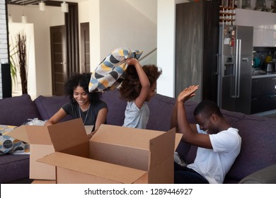 Happy african child laugh enjoy funny pillow fight with american parents at home, happy joyful kid daughter play with black family having fun pack unpacking boxes on moving day, relocation, mortgage - Powered by Shutterstock