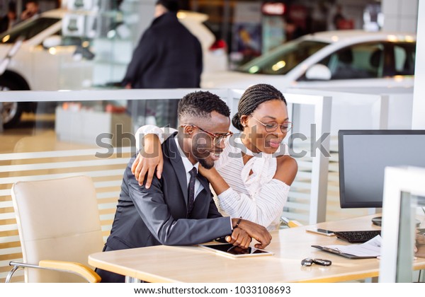 happy African couple and female seller sit at\
table and make a deal for sale of\
car