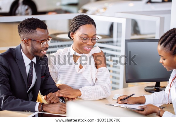 happy African couple and female seller sit at\
table and make a deal for sale of\
car