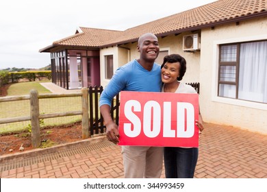 Happy African Couple Standing Outside Their House And Holding Sold Sign