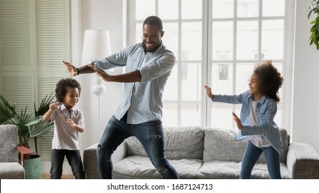 Happy African Ethnicity Father Have Fun Teaches Little Preschool Kids To Dance In Modern Living Room At Home. Dad With Son And Daughter Engaged In Funny Activity Enjoy Leisure Carefree Weekend Concept