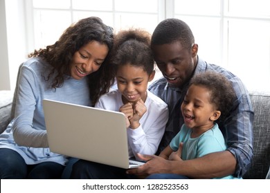 Happy African Family With 2 Children Having Fun Using Laptop Together At Home, Black Parents And Little Kids Watching Funny Video, Doing Online Shopping, Making Video Call Looking At Computer Screen