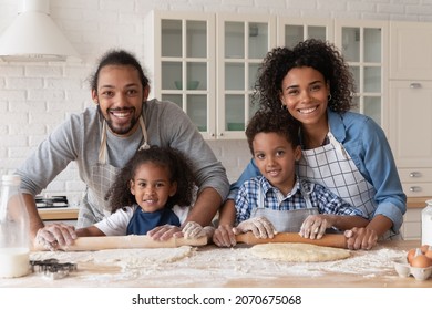 Happy African Family Baking Dessert For Dinner Together. Sibling Children Helping Couple Of Parents To Cook, Rolling Dough On Table With Flour Messy, Looking At Camera, Smiling, Head Shot Portrait