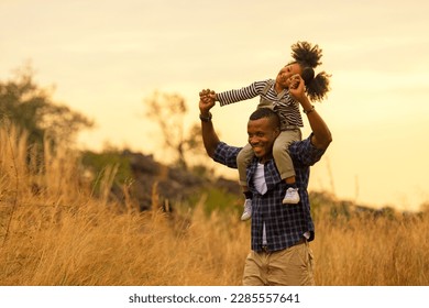 Happy African family child daughter riding the neck father and running on meadow nature on silhouette lights sunset.  Travel and Family Concept - Powered by Shutterstock