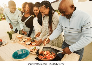 Happy african family cooking outdoor at home rooftop terrace during summer time - Sunday dinner community concept - Focus on mother face - Powered by Shutterstock