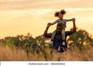 Happy African Family Father And Child Daughter Travel And Running On Meadow Nature On Silhouette Lights Sunset.  Travel And Family Concept