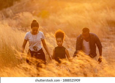 Happy African Family Father And Child Daughter Travel And Running On Meadow Nature On Silhouette Lights Sunset.  Travel And Family Concept