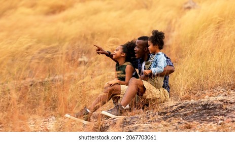 Happy African family father and child daughter travel and sitting pointing on meadow nature on silhouette lights sunset.  Travel and Family Concept