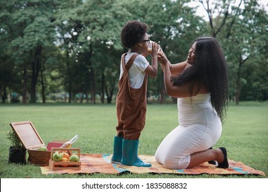 Happy African family Mother and son picnic together at garden green park on weekend. Young mom holding a glass of milk for her kid to drink - Powered by Shutterstock