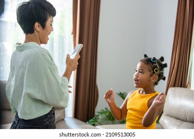 Happy African Family Mother Using Smartphone With Mobile Application Making Viral Video Content Or Live Streaming With Dancing Little Child Girl Daughter In Living Room. People And Technology Concept.