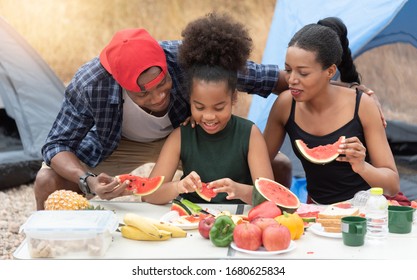 Happy African Family Relaxing On A Camping Trip At A Autumn Outdoor. Smiling Black Mom, Dad, Daughter Enjoying And Eating Watermelon On Holiday Picnic Together.