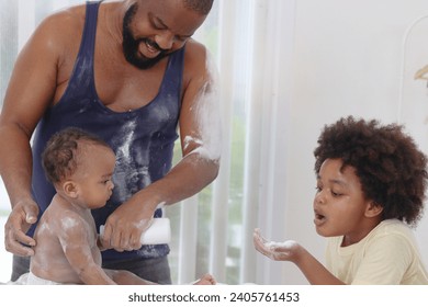 Happy African family, toddle baby infant sits on towel after takes a bath in bathroom, father and son brother hold dusting powder bottle and apply talcum powder on body of little kid daughter child. - Powered by Shutterstock