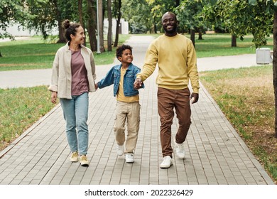 Happy African family walking together with their little son in the park, they holding hands and going through the street
