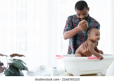 Feliz padre africano con barba bañando a una adorable bebé recién nacida en bañera en casa. Papá limpiando a su pequeña niña con esponja en agua caliente. Concepto de cuidado de la limpieza de la higiene infantil