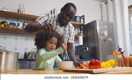 Happy African Father And Daughter Making Dough For Pizza Having Fun Together In Kitchen Indoors. Portrait Of Afro Dad Helping Cute Little Girl Mixing Eggs Preparing Dinner Together