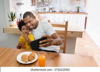 Happy African Father And Son Taking Selfie With Smartphone During Lunch Time In Kitchen Room. Portrait Smiling Dad And Little Kid Boy Making Video Call With Mobile Phone Together At Home. Black Family