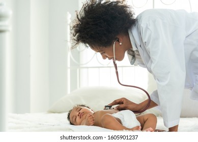 Happy african female doctor examining baby boy with female nurse on background