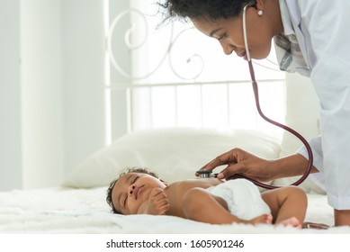 Happy african female doctor examining baby boy with female nurse on background