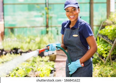 happy african female nursery worker watering plant - Powered by Shutterstock