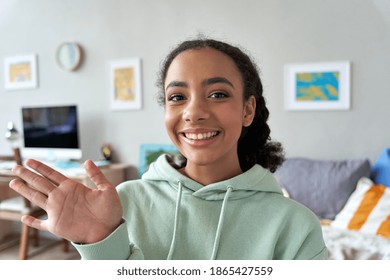 Happy african gen z teen girl waving hand talking to camera in bedroom. Mixed race teenager recording vlog, streaming for social media, video calling in online chat at home. Web cam view headshot