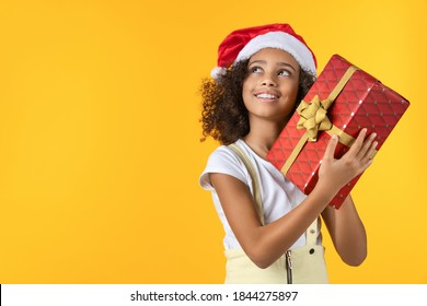 Happy African Girl In Christmas Hat Holding Present Box Isolated On Yellow Background