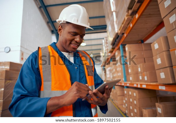 Happy african industrial staff using digital\
tablet in large warehouse