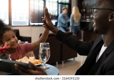 Happy African little daughter raise hand gives high five to dad while enjoying time together at airport departure lounge . Black father holding digital tablet while waiting for flight. - Shutterstock ID 2164191133
