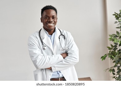 Happy african male doctor wearing white coat, stethoscope looking at camera standing with arms crossed in medical office. Smiling black man professional therapist physician posing at work, portrait.