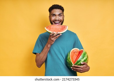 Happy African man eating watermelon while standing against yellow background - Powered by Shutterstock