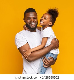 Happy african man embracing his positive little daughter, orange studio background - Powered by Shutterstock