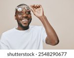 Happy African man with glasses, joyful expression, wearing casual white t shirt, beige background, showcasing excitement and positivity in a friendly atmosphere