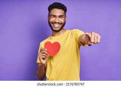 Happy African man holding paper heart and smiling while standing against purple background - Shutterstock ID 2176785747
