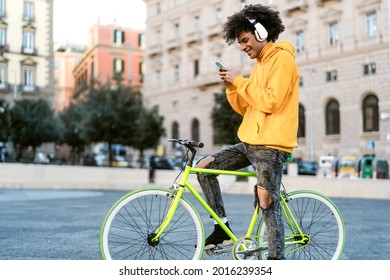 Happy African Man Using Mobile Smartphone Outdoor - Young Guy Having Fun Riding With Bike In The City - Youth Millennial Generation Lifestyle And Technology Concept