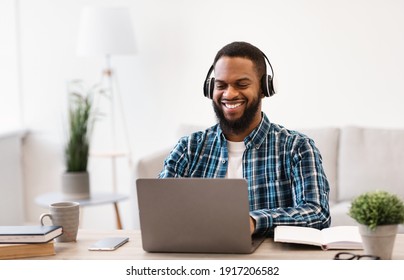 Happy African Man Working On Laptop Wearing Headphones Sitting At Workplace In Modern Office. Business And Entrepreneurship, Successful Career And Distance Job Concept. Selective Focus - Powered by Shutterstock