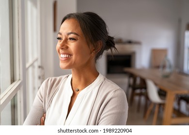 Happy african mature woman standing near window while looking outside. Cheerful mid adult woman looking through the window at home with a big smile. Smiling black lady standing and laughing. - Shutterstock ID 1989220904