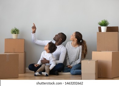 Happy African Mixed Race Ethnicity Family Discuss New Home Renovation Sit On Floor Relocating In Own Apartment With Boxes, Parents And Cute Child Son Talk Enjoy Moving Day Mortgage Investment Concept