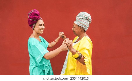 Happy african mother and daughter dancing together while wearing traditional clothes - Motherhood, music, ethnic cultures and family concept - Focus on faces - Shutterstock ID 2354442013