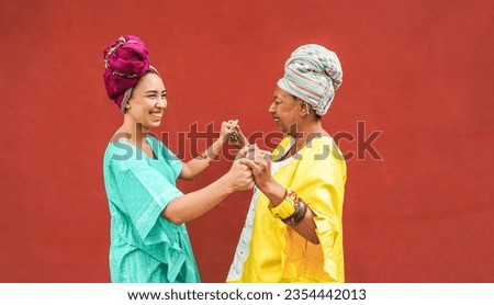 Happy african mother and daughter dancing together while wearing traditional clothes - Motherhood, music, ethnic cultures and family concept - Focus on faces