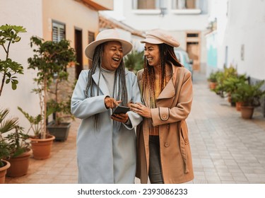 Happy african mother and daughter having fun together using mobile phone in the city during winter time - Travel and vacation concept - Powered by Shutterstock