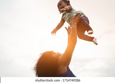 Happy african mother playing with her daughter outdoor - Afro mum and child having fun together - Family, happiness, real people and love concept - Focus on mom face
