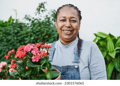 Happy african senior woman smiling on camera while holding flowers at home terrace - Gardening concept - Powered by Shutterstock