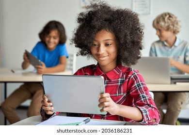 Happy African teen school girl holding device using digital tablet computer at class in classroom. Smiling black junior school student learning online education program app technology during lesson. - Powered by Shutterstock